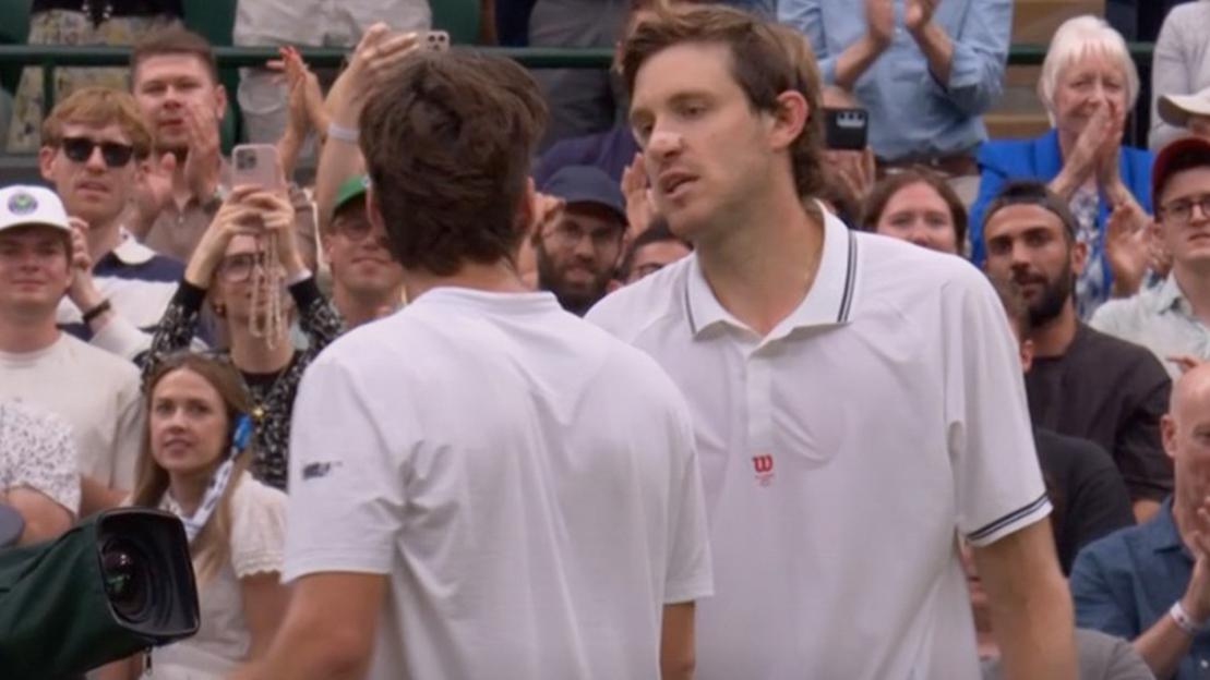 Two tennis players in white shirts stand among spectators.