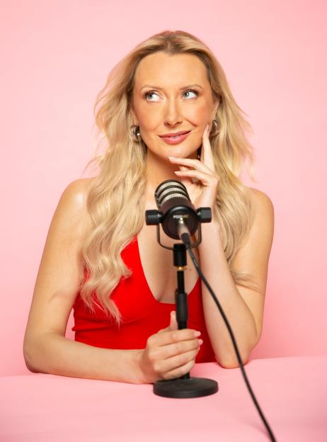 Woman in red dress sits at pink table with microphone.