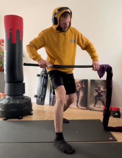 Man in a yellow hoodie practicing martial arts with a bo staff.