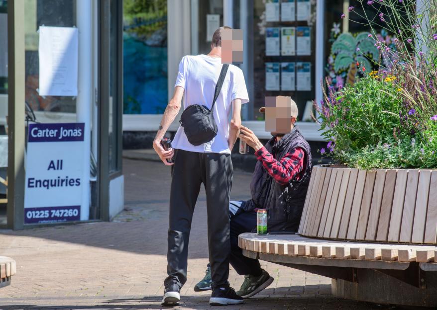 Two people sitting on a bench, one holding a can.