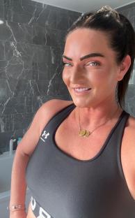 Woman in a black sports bra smiling in a bathroom.