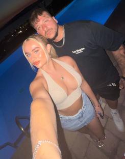 A young couple poses for a selfie by a swimming pool at night.