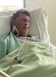Man in hospital bed with IV and nasal cannula.