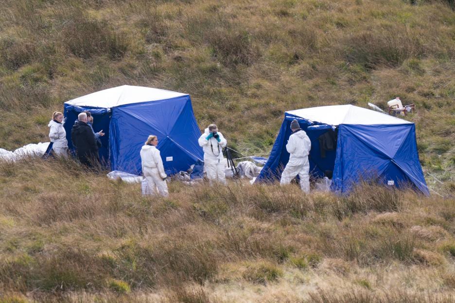 Police officers in white suits searching a field.