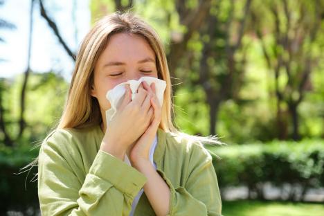 Woman blowing her nose with a tissue in a park.