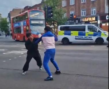 Two people fighting in the street near a police van.