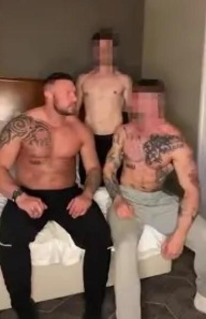 Three shirtless men sitting on a bed; text overlay accuses them of profiting from the LGBTQ+ audience while claiming to be straight.