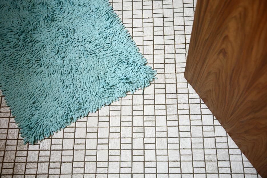 Turquoise bath mat on tiled bathroom floor.
