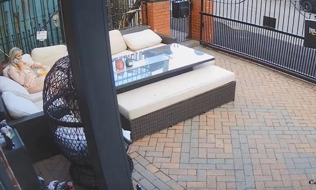 Security camera footage of a woman on a patio, on a phone call.