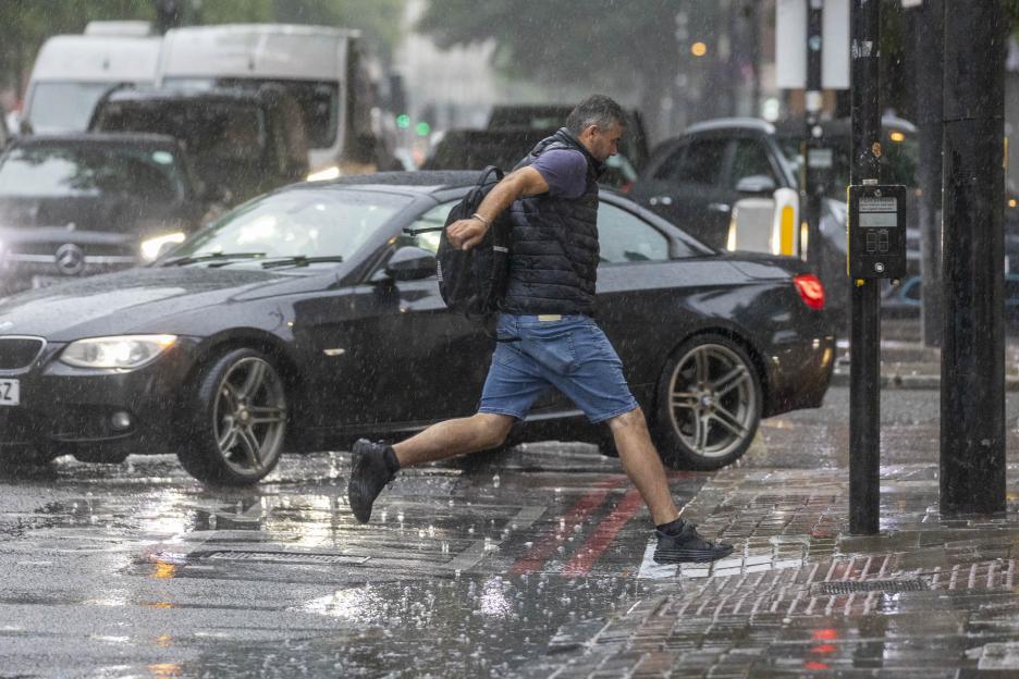 Man jumping over a puddle in heavy rain.