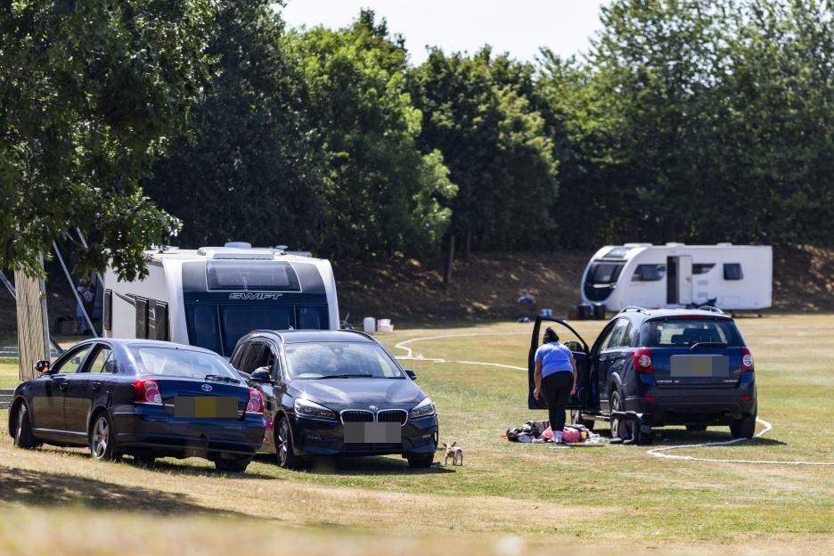 Travellers' caravans and cars parked on a sports field.