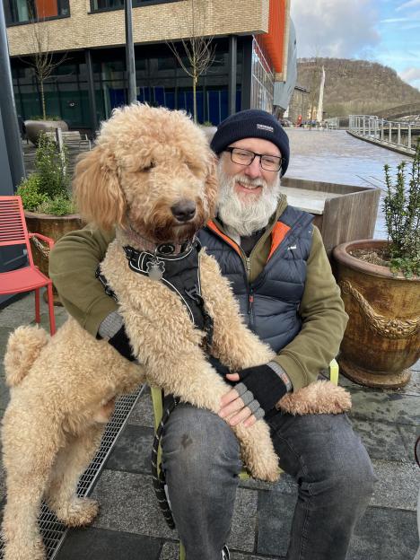 A man holding a large Bernedoodle dog on his lap.