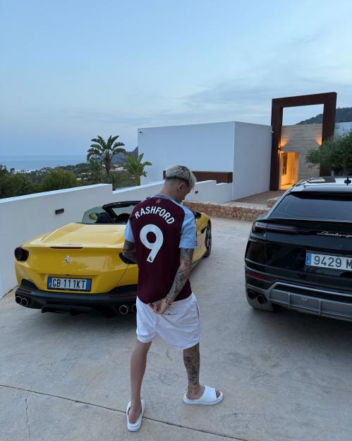 Man in Rashford jersey standing between a yellow Ferrari and a black Lamborghini.