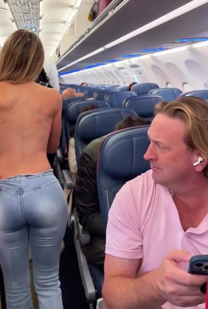 Woman in low-cut jeans walking down airplane aisle.