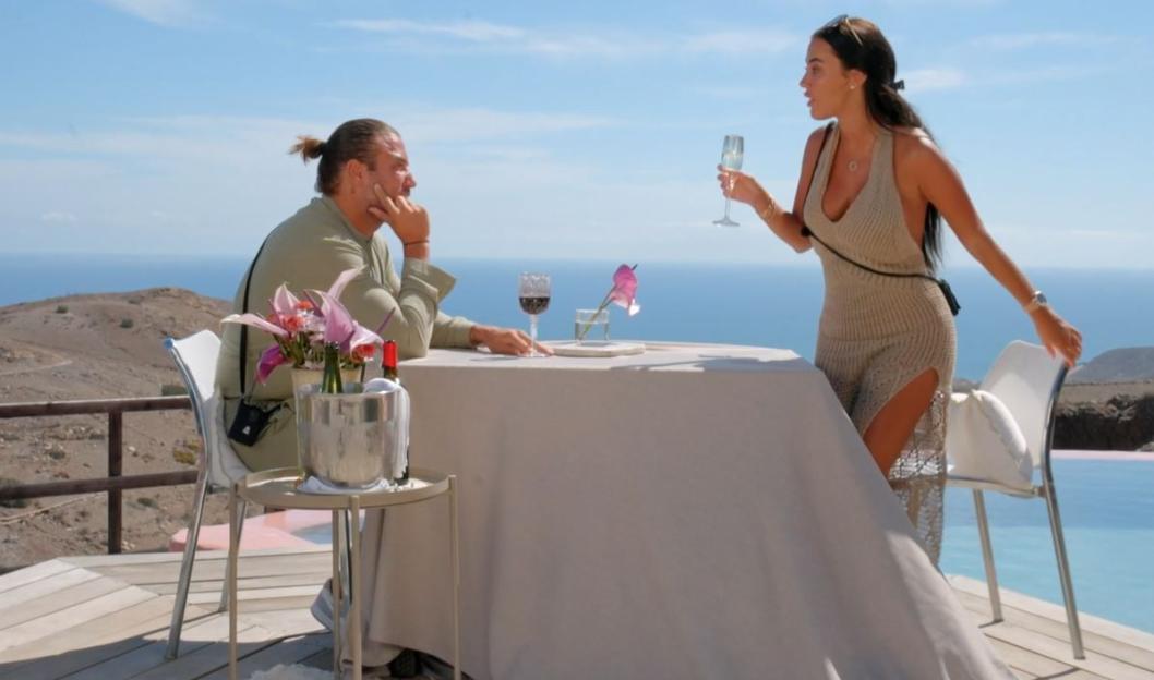 Couple having a tense conversation at an outdoor table overlooking the ocean.
