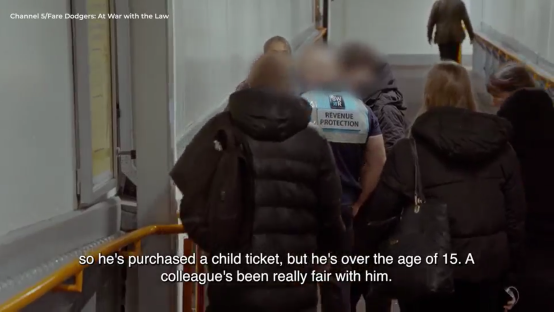 Screenshot of people walking down a corridor; one person wears a