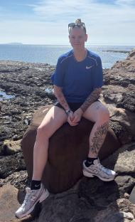 Woman with tattoos sitting on a rock by the ocean.