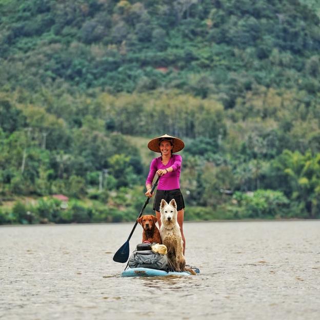 Woman stand-up paddleboarding with two dogs.