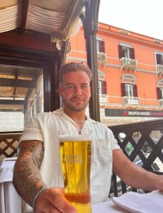 Man holding a beer glass at an outdoor cafe.