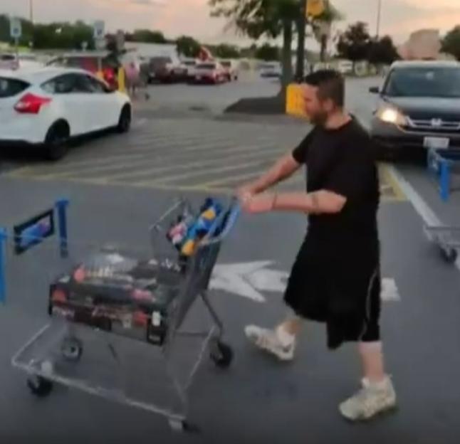 Man pushing a shopping cart in a parking lot.