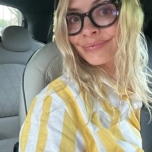 Woman wearing glasses and a yellow striped shirt in a car.