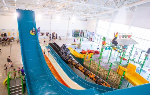 Aerial view of an indoor water park with slides and a splash pad.