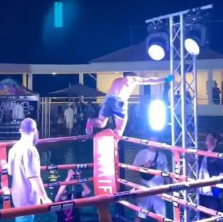 A boxer falling backwards out of a boxing ring into a pool.