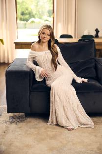 Woman in a white lace dress sitting on a couch.