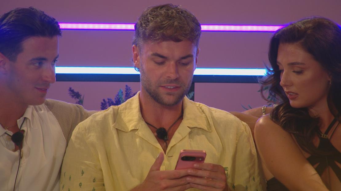 Three Love Island contestants looking at a phone.