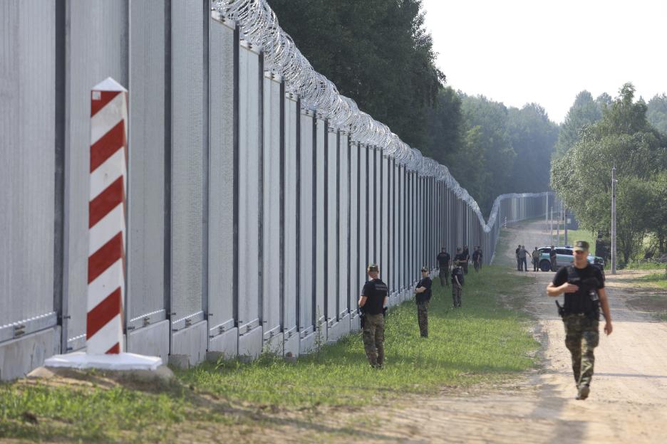 Polish border guards patrolling a metal wall on the Poland-Belarus border.