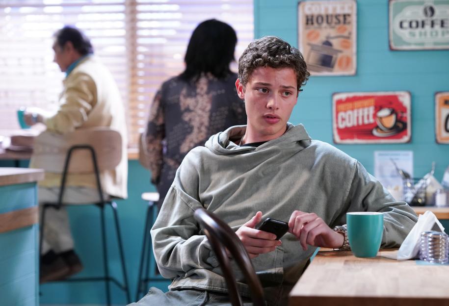 Bobby Brazier as Freddie Slater in EastEnders, looking at his phone in a cafe.