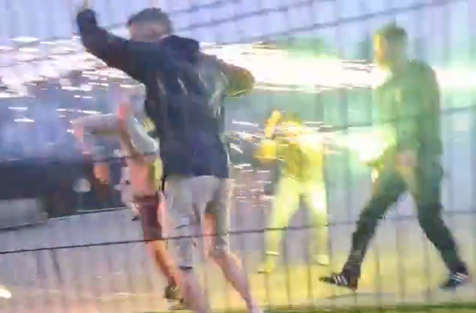 People setting off fireworks near a fence.