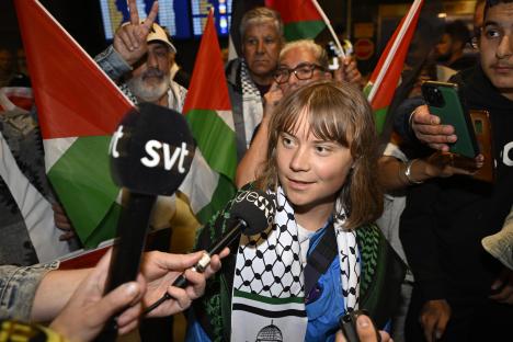 Greta Thunberg speaks to journalists at an airport, surrounded by Palestinian flags.