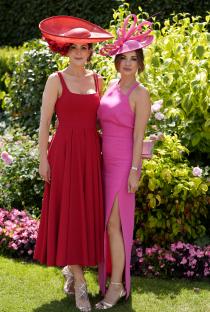 Two women in red and pink dresses and hats at a horse race.