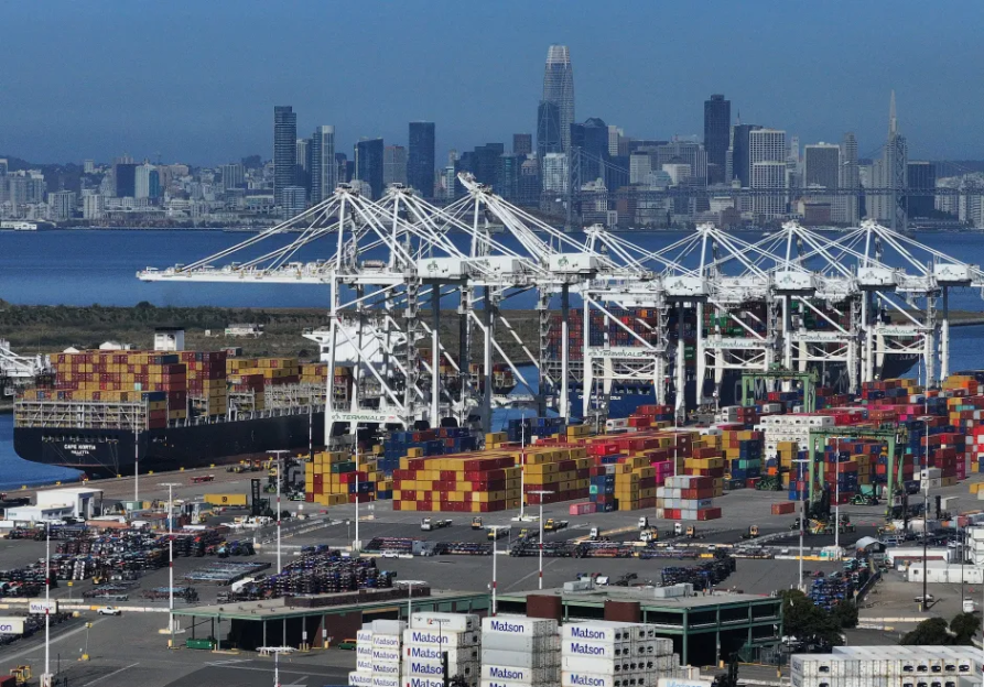 Container ship at port with city skyline in background.
