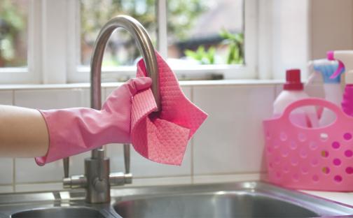 Person wearing pink gloves rinsing a pink cleaning cloth under a kitchen tap.