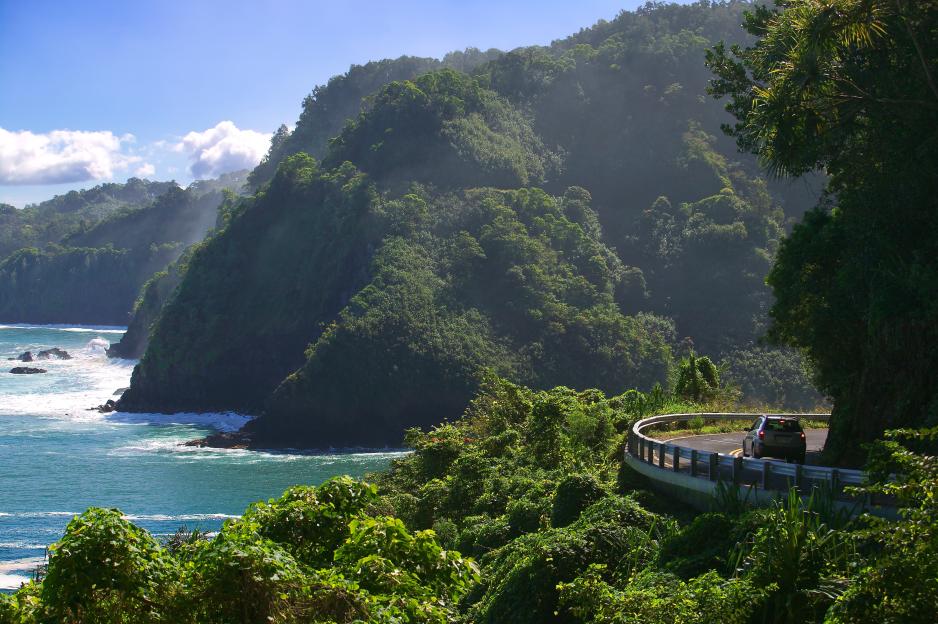 Car driving on a coastal road with ocean and cliffs.