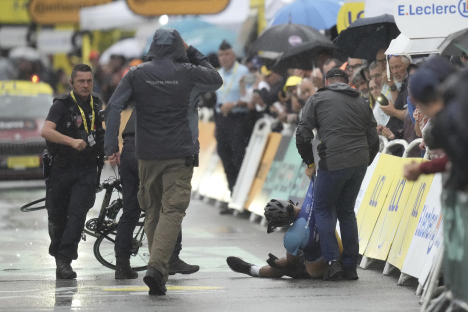 Cyclist lying on the ground after a crash during a race, attended to by security and race officials.