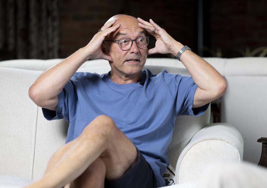 Gregg Wallace sits on a couch, looking surprised, hands on his head.