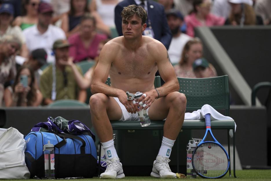 Jack Draper of Britain sits on a bench during a tennis match, shirtless and holding a water bottle.