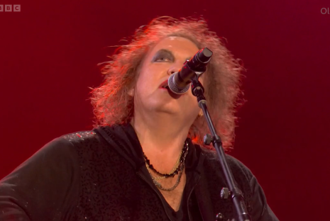 Robert Smith of The Cure singing into a microphone.