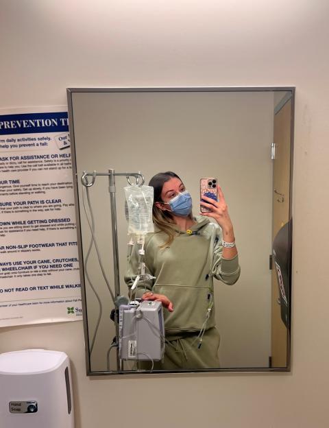 Woman in pink sweats standing next to an IV pole.