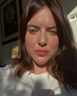Close-up selfie of a woman with brown hair wearing a white shirt and necklace.