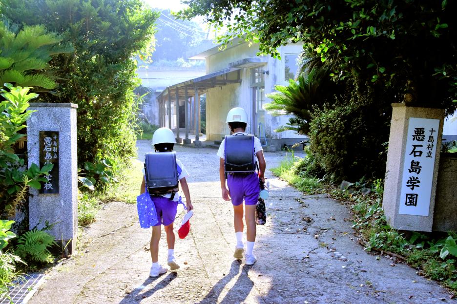 Two children wearing helmets and backpacks walk to school.