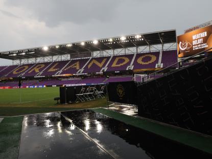 Wet soccer stadium with weather delay announced on scoreboard.