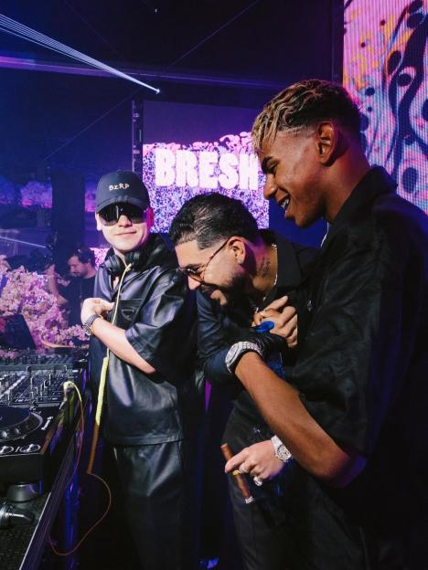 Three men at a nightclub, one DJing.