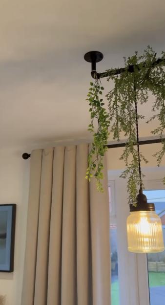 Hanging light fixture with greenery near beige curtains.