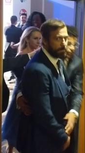 A man in a suit escorts a woman through a doorway.