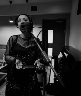 Shona McGarty singing into a microphone in a recording studio.