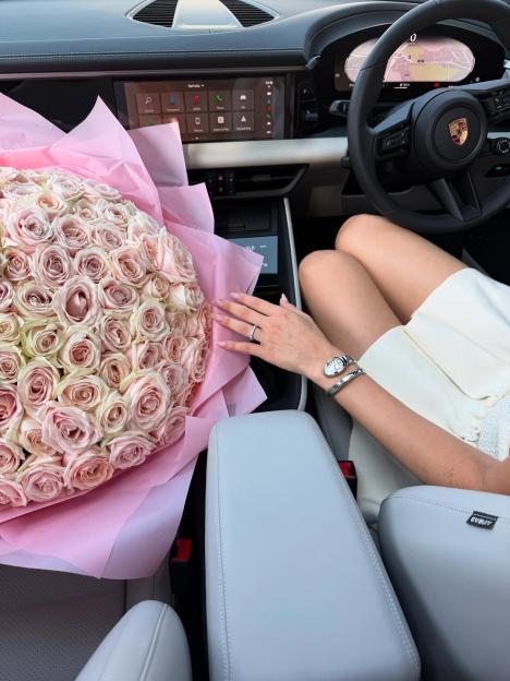 A woman in a Porsche with a large bouquet of light pink roses.
